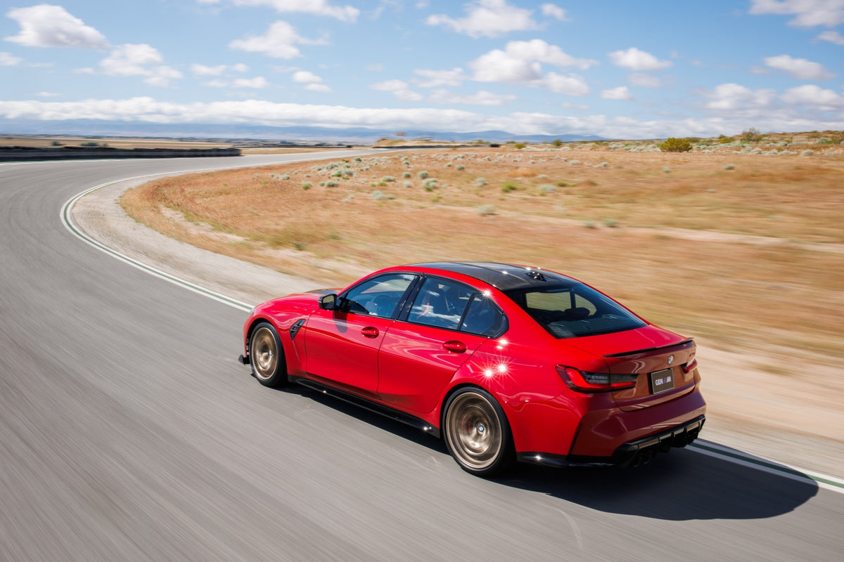 Red BMW M3 CS Handschalter driving on a circuit, viewed from the rear three-quarter angle