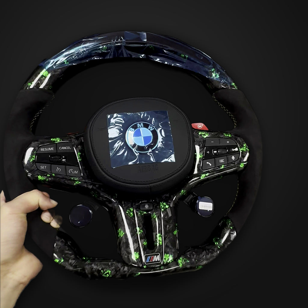 Green-flake forged carbon and Alcantara BMW G-Series M steering wheel held in hand